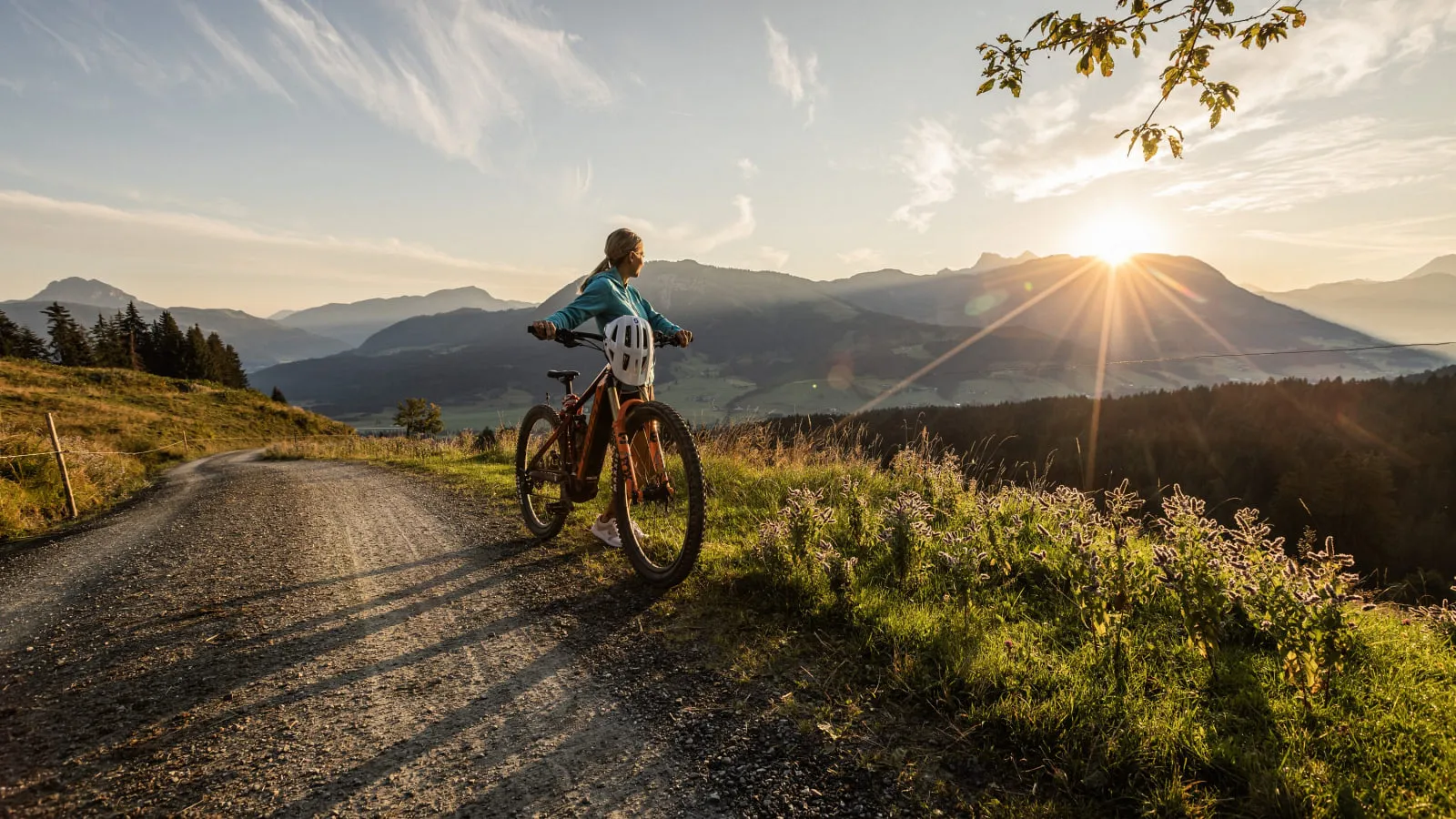 Radfahrerin auf einem Schotterweg bei Sonnenuntergang über den Bergen