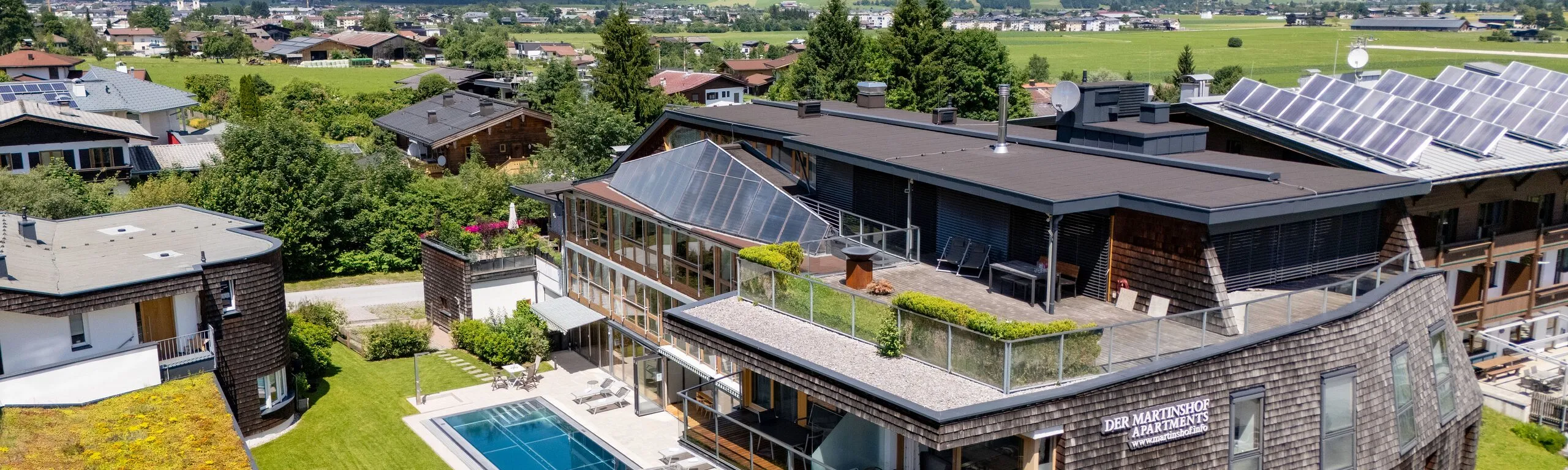 Luftaufnahme des Martinshofs mit Pool, dahinter der Wilde Kaiser